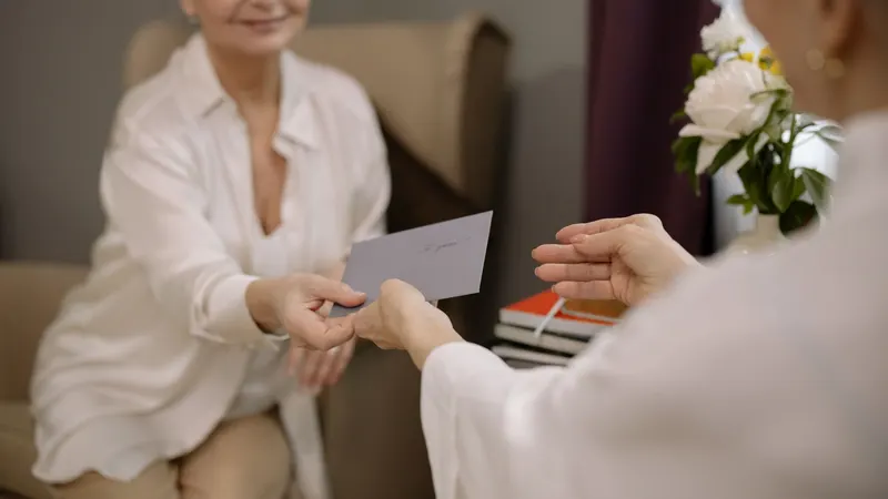 Starsza kobieta w fotelu wręcza kopertę drugiej osobie, darowizna od rodziców, która po rozwodzie zostaje majątkiem osobistym