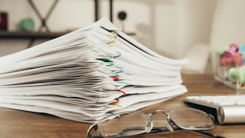 Stos dokumentów spiętych spinaczami i okulary na biurku, sprawdzanie długów spadkowych po zmarłym